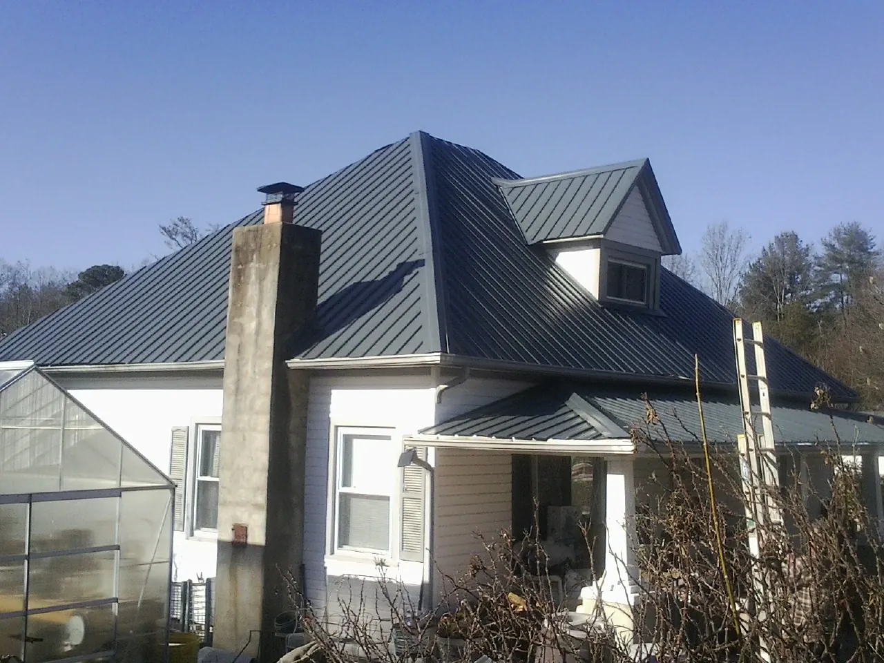 Dark blue standing seam metal roof on a white farmhouse with dormer — Slate & Tile Roof Repair by Roofing Brothers in Aransas Pass