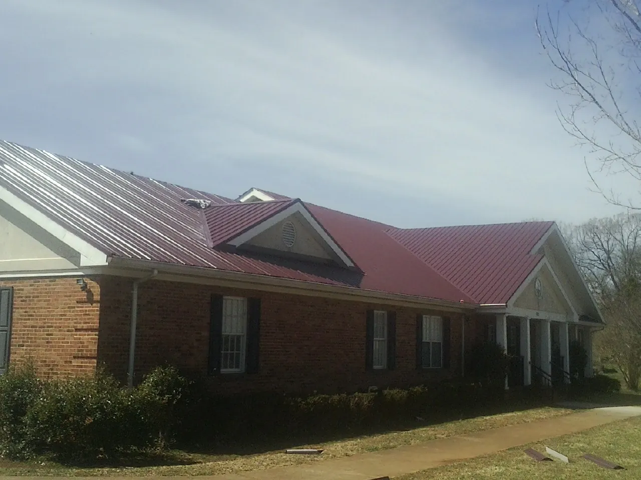 Red metal roof with gabled entries on a long brick building, from a Hail Damage Roof Repair job in Aransas Pass
