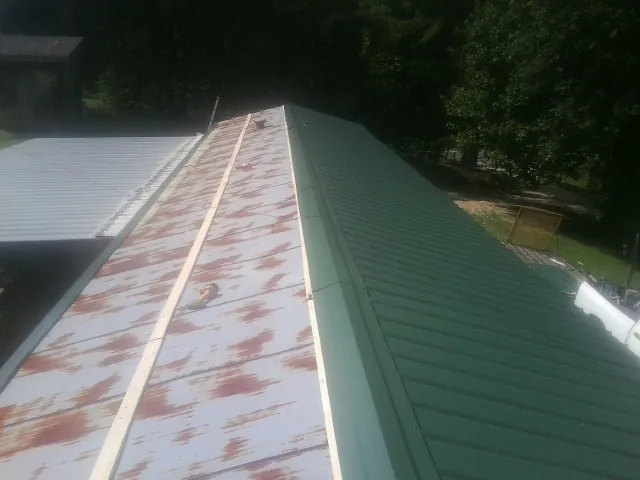 Old rusted panels beside newly installed green metal roofing — Wind Damage Roof Repair by Roofing Brothers in Aransas Pass