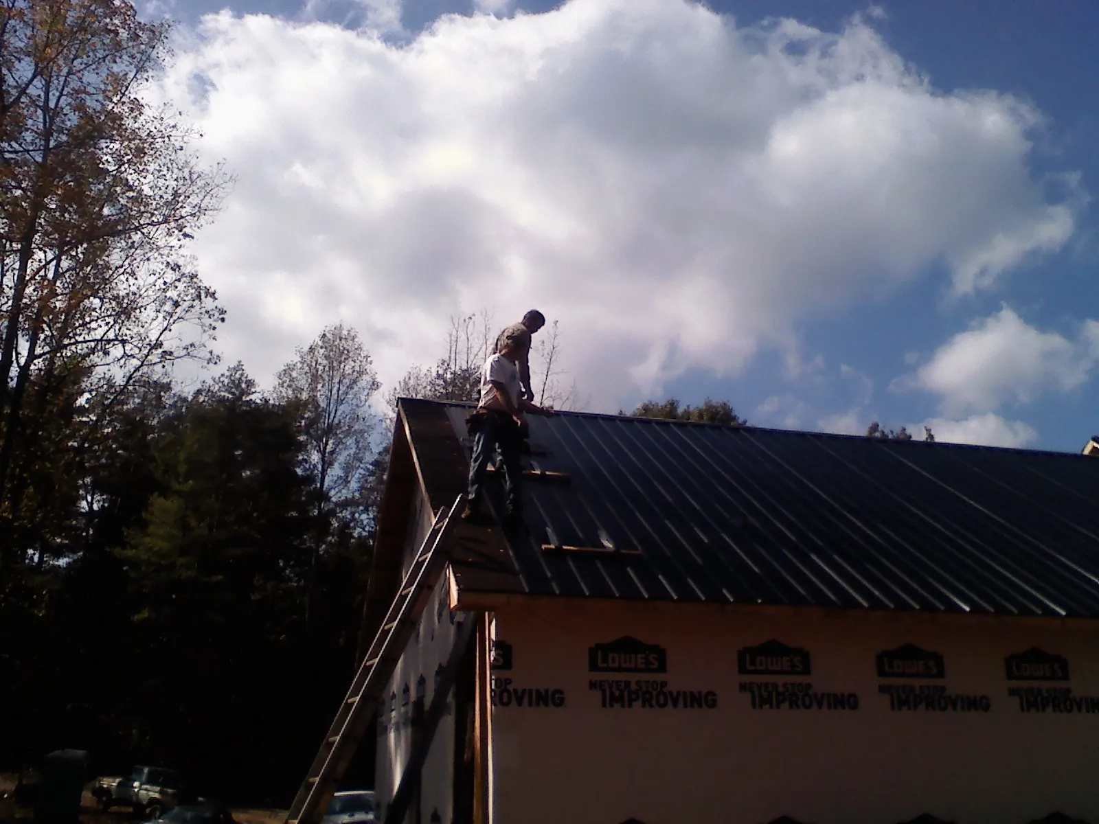 Roofer fastening dark metal panels high against a cloudy sky, from a Roof Inspection job in Aransas Pass