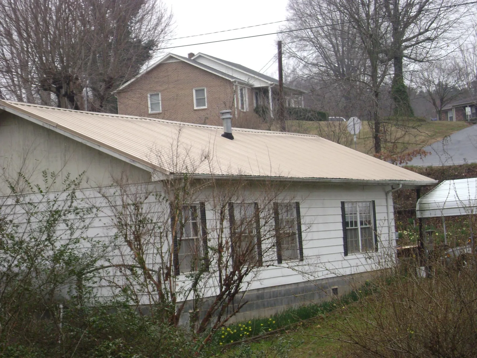 Tan metal roof on a white sided house set into a hillside — Commercial Roofing by Roofing Brothers in Aransas Pass